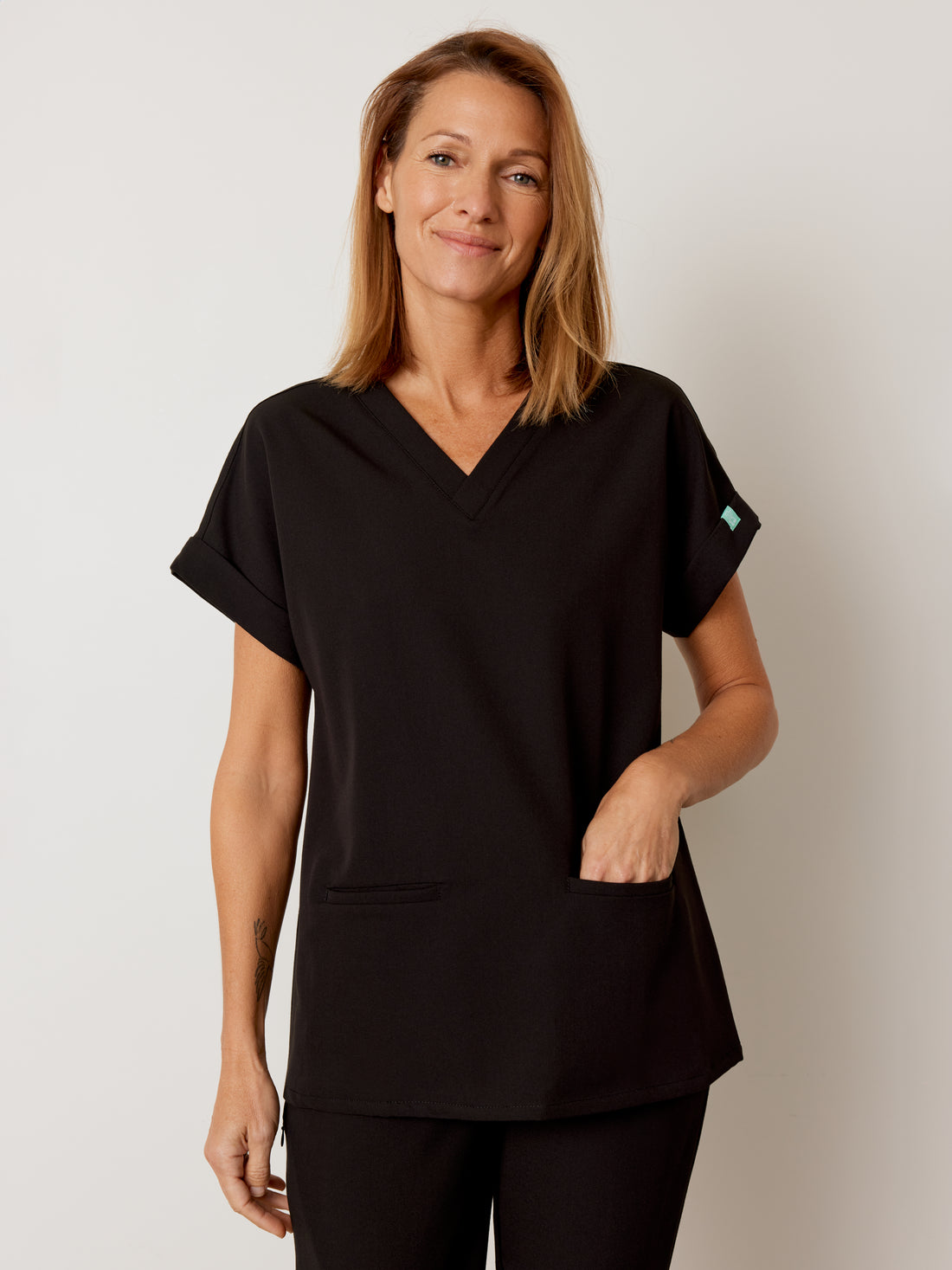 Woman wearing a black scrub top with a small logo on a plain background