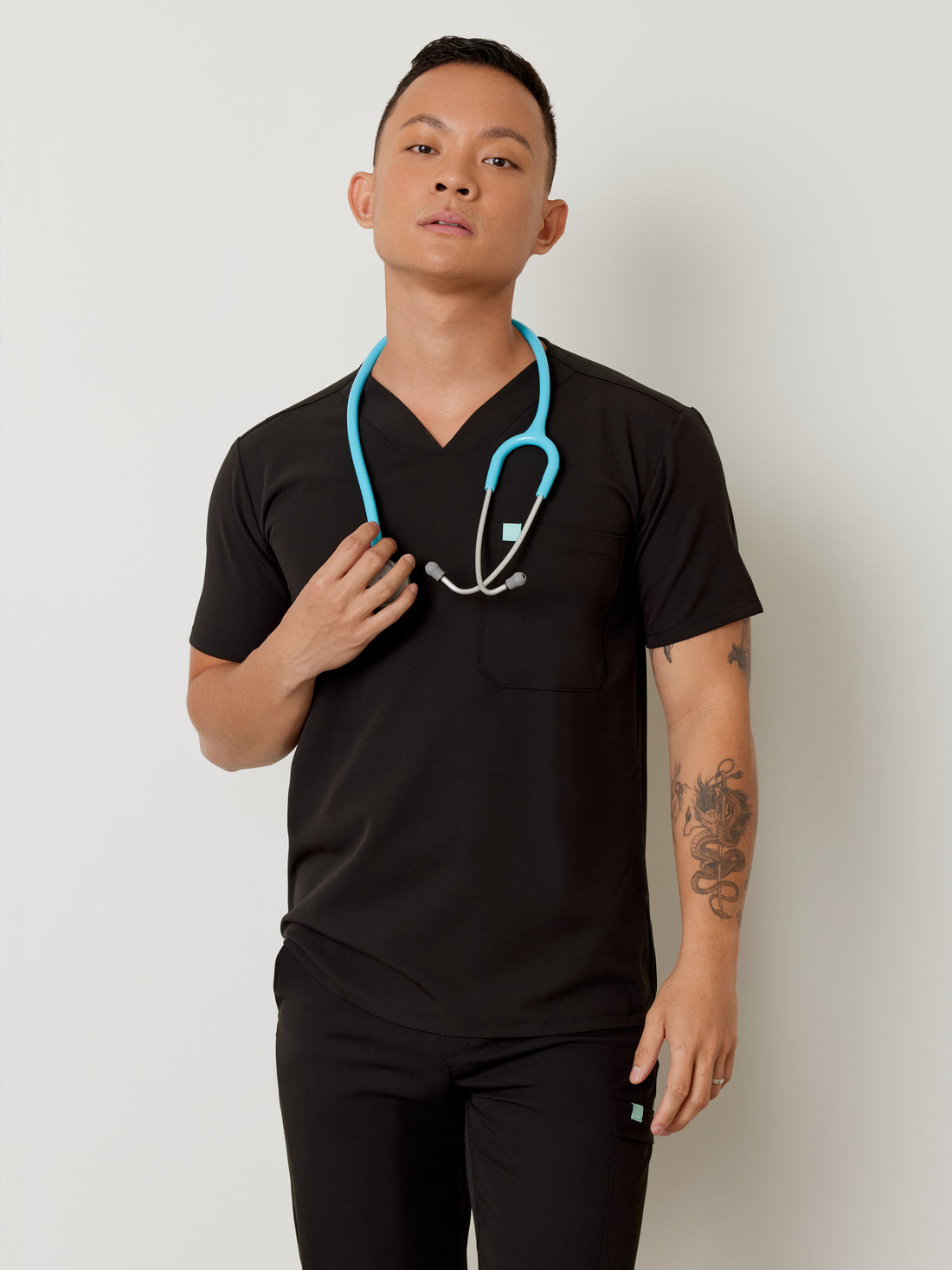 A person wearing a black one-pocket scrub top with a modern V-neck, featuring side stretch panels.