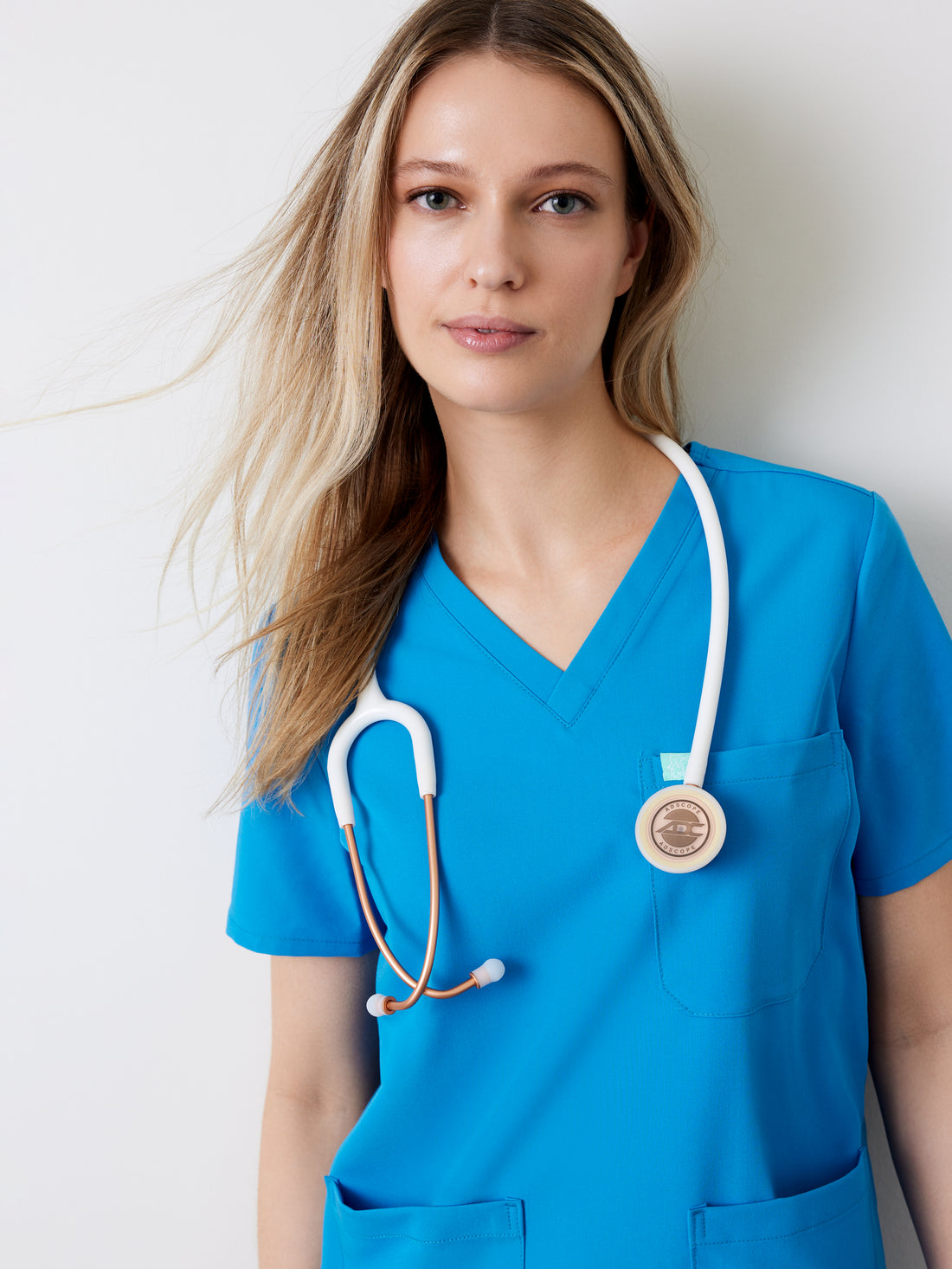 A woman wearing a blue V-neck scrub top with three pockets, paired with a stethoscope around her neck.
