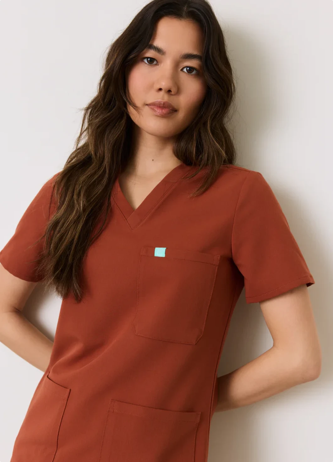 Woman wearing a rust-colored scrub top with a small blue logo on a white background